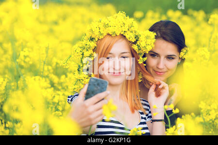 Due amici prendendo un selfie in un campo di fiori gialli di semi di colza Foto Stock