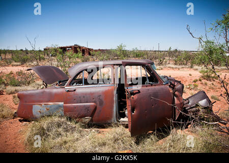 Abbandonato arrugginita auto con fori di proiettile nel campo deserto Foto Stock