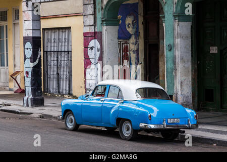 Un blu e bianco auto classica è parcheggiata da un certo numero di coloratissimi murales sui pilastri di un edificio sul Prado a l'Avana. Foto Stock