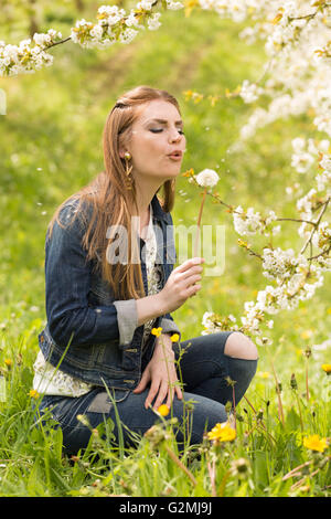 Una bruna giovane donna dai capelli in jeans godendo i primi giorni di primavera in un verde prato circondato da ciliegi fioriti Foto Stock