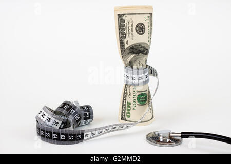 Un mazzetto di fatture del dollaro serrare mediante un nastro di misurazione e uno stetoscopio su sfondo bianco Foto Stock