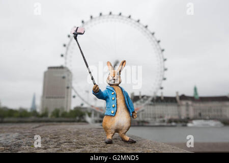 Solo uso editoriale una scultura in miniatura di Beatrix Potter personaggio Peter Rabbit prendendo un selfie vicino al London Eye a Londra, che è stato aggiornato per il XXI secolo da artista di strada Marcus Crocker nella celebrazione del centocinquantesimo anniversario dell'autore della nascita. Foto Stock