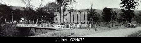 La fotografia mostra un certo numero di soldati indonesiani a piedi attraverso un villaggio , attraverso un ponte, armati di mitragliatrici. Le Indie orientali olandesi, noto come Indonesia moderna. Datata c1935. Foto Stock