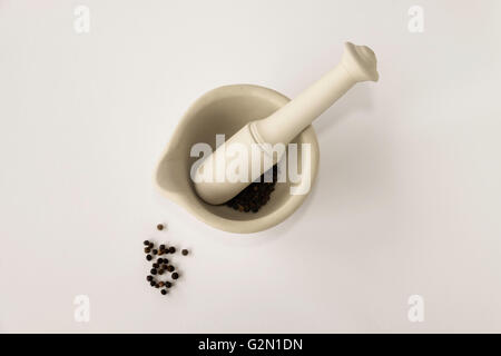 Lay immagine piatta della ceramica mortaio e pestello con pepe nero su sfondo bianco Foto Stock