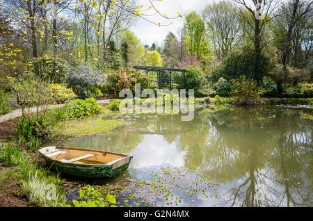 Ampio giardino sul lago con il vecchio legno barca a remi in un giardino privato in Cornovaglia Foto Stock