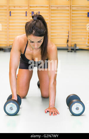 Giovane donna fa pushups con sumbbells in palestra Foto Stock