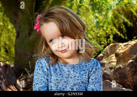 Un simpatico bambina si siede sotto un albero di Mesquite e guarda al di fuori della fotocamera con un "Stai scherzando?" espressione. Foto Stock