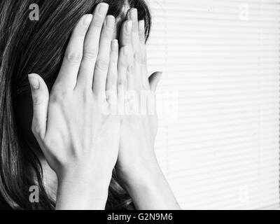 Ritratto bianco e nero di una giovane donna che copre il suo volto in vergogna o imbarazzo Foto Stock