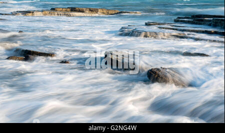 Le onde del mare si infrangono su piatti di mare rocce creando piccole cascate e liscia i flussi di acqua. Foto Stock