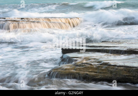 Onde si infrangono con potenza su una spiaggia rocciosa Foto Stock