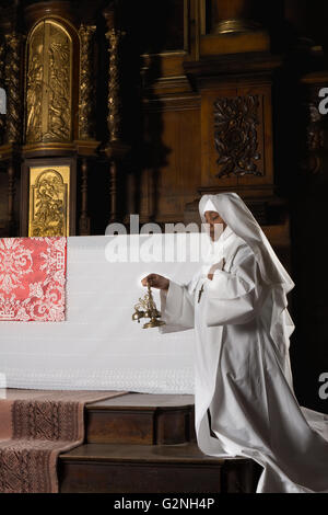 Nun squillo campane di rame durante la messa cattolica al momento della consacrazione in una chiesa del XVII secolo interno Foto Stock