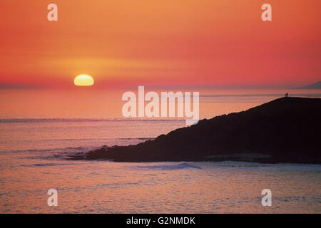 2 La gente guarda il sole di setting da un promontorio circondato dal mare colorato di rosso dal cielo di sera Foto Stock