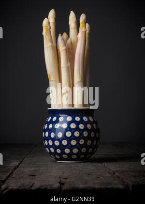 Freschi asparagi bianchi in un rustico vaso blu su una tavola di legno Foto Stock