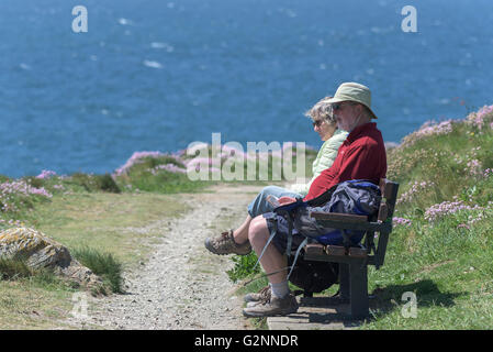 Tempo soleggiato come due escursionisti Godetevi un riposo su un banco di lavoro su East Pentire in operazioni automatiche di fine campo, Newquay Cornwall. Foto Stock