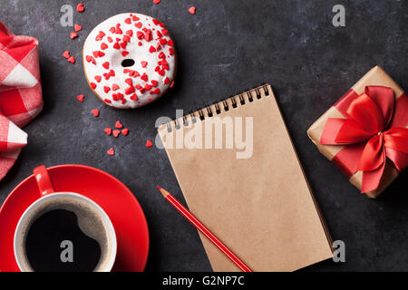 Ciambella, caffè e confezione regalo sul tavolo di pietra. Vista da sopra con il blocco note per lo spazio di copia Foto Stock