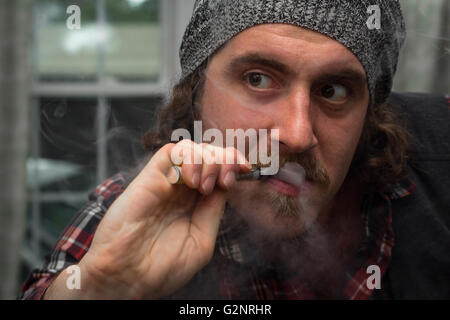 Capelli lunghi uomo barbuto fuma una vape e-sigaretta Foto Stock