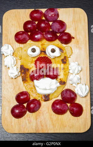 Simpatiche faccia fatta di fettine di uva, fragole e pancake, come visto da sopra Foto Stock