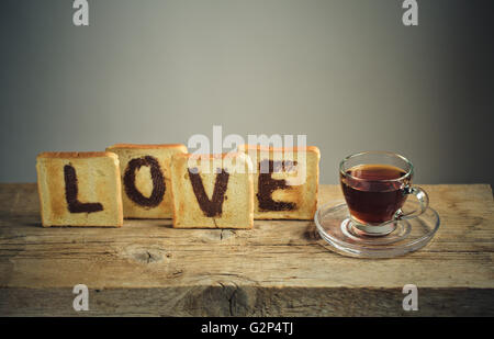 Tostare il pane con la parola amore dipinto con granella di nocciole cioccolato da spalmare e una tazza di tè Foto Stock