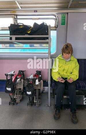 Una donna più anziana viaggi in treno con Brompton biciclette e bagagli in un carrello progettato per il trasporto di biciclette. Foto Stock