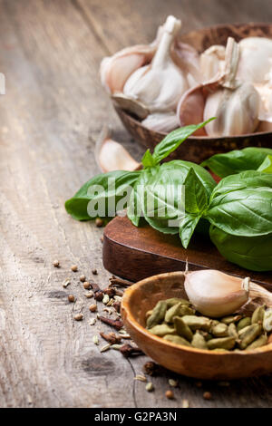 Il basilico, l'aglio, spezie: cardamomo, chiodi di garofano e pepe nero sul vecchio sfondo di legno Foto Stock