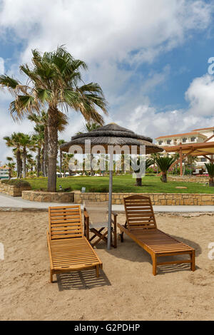 Lettini in legno e paglia ombrello per il relax sul mare Mediterraneo spiaggia di sabbia a Paphos, Cipro. Foto Stock