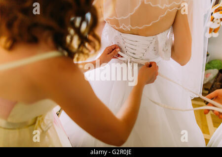 Bridemaiden aiuta a vestire sposa il suo bianco abito da sposa Foto Stock