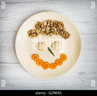 Divertente faccia fatta di carota, biscotti e noci sulla piastra. L'espressione del viso. Crazy tema. Cucina creativa. Cibo sano. Umorismo Foto Stock