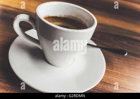 Caffè appena macinato di caffè nella tazza bianca sul piattino con cucchiaio. Primo piano con messa a fuoco selettiva e vintage correctio tonale Foto Stock