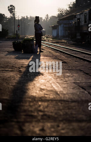 Silhouette di una donna con il suo bagaglio di attesa per il treno, Yangon Stazione Ferroviaria Centrale, Myanmar. Foto Stock