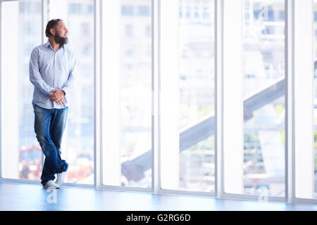 Corpo pieno colpo di uomo con la barba a guardare fuori dalla finestra Foto Stock