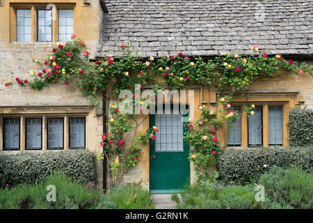 Cotswold cottage in pietra con il rosso e il giallo di rose. Stanton, Cotswolds, Gloucestershire, Inghilterra Foto Stock