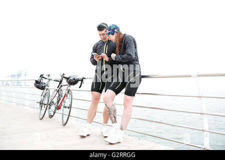 Bella coppia Giovane con le bici in piedi sul molo e utilizzando il telefono cellulare insieme Foto Stock