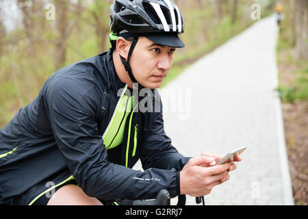 Giovane serio in moto il casco con bicicletta utilizzando il telefono cellulare Foto Stock