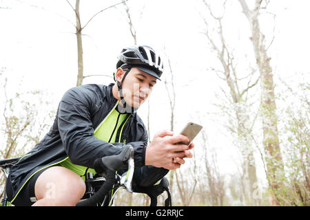 Bel giovane uomo nel ciclismo casco con la bicicletta utilizzando lo smartphone nel parco Foto Stock