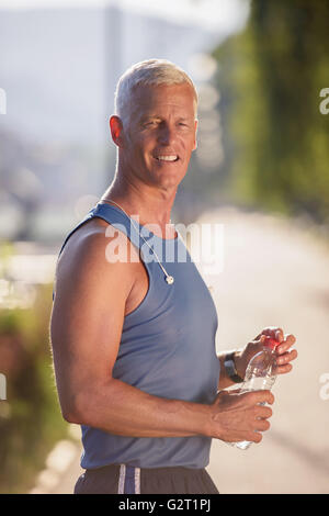 Bello il senior jogging uomo di bere acqua fresca da una bottiglia dopo mornig eseguire Foto Stock