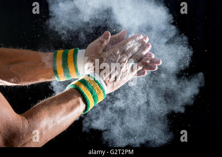 Nastrato mani del ginnasta indossando i colori del Brasile di braccialetti battimani bianco gesso in polvere in una nuvola contro uno sfondo scuro Foto Stock