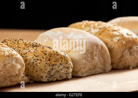 Pane appena sfornato e seminato pane integrale rotoli allineati su una breadboard di legno Foto Stock