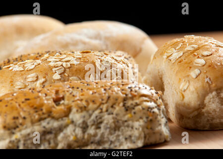 Close up e una selezione di fresche seminate pane integrale rotola su una breadboard di legno Foto Stock