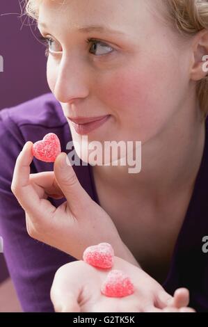 Giovane donna mangiare rivestite di zucchero, a forma di cuore caramelle gommose Foto Stock