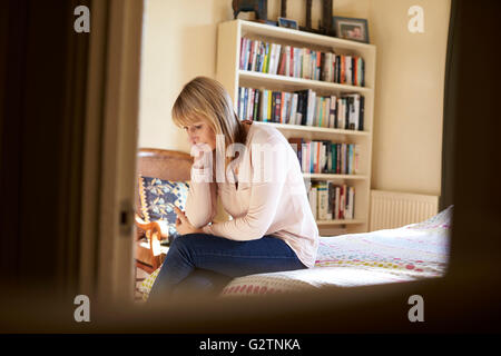 Premuto donna matura seduta sul letto di casa Foto Stock