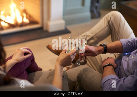 Chiusura del giovane seduto da Fire rendendo Toast Champagne Foto Stock