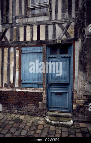 Weathered blue door e otturatore sull esterno del vecchio edificio con travi di legno sulla strada di ciottoli in Honfleur, Francia Foto Stock