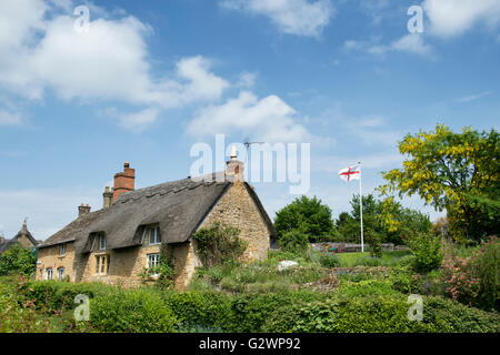 Cottage con tetto in paglia e la bandiera inglese nella Ebrington, Chipping Campden, Gloucestershire, Inghilterra Foto Stock