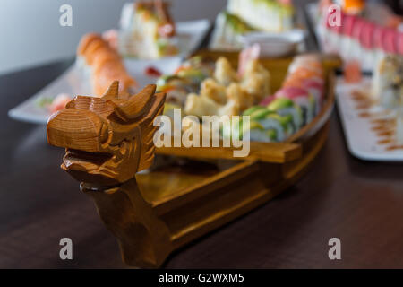 Varietà di rotoli di sushi servita su una barca di legno Foto Stock