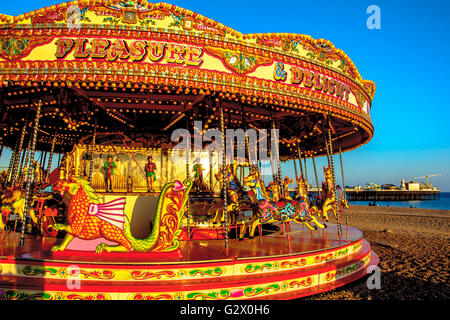 Una giostra sulla spiaggia di Brighton con pier su sfondo, East Sussex, Inghilterra Foto Stock