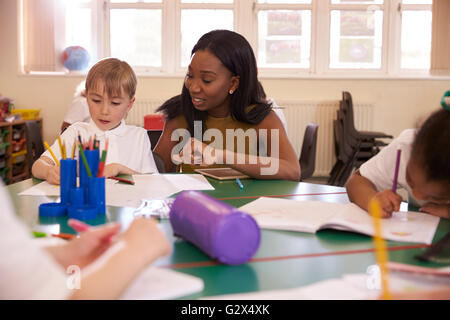 Insegnante di scuola elementare aiutando pupilla maschio alla scrivania Foto Stock