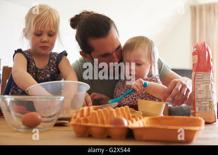 Padre con le figlie a casa Cottura di torte insieme Foto Stock