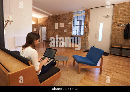 Donna che lavorano da casa su computer portatile in moderno appartamento Foto Stock