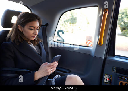 Imprenditrice viaggiare in taxi tramite telefono cellulare Foto Stock