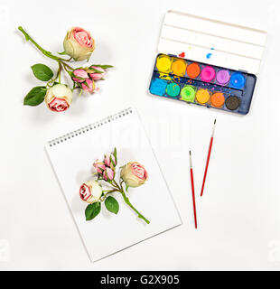 Sketchbook, acquerello, spazzole, carta, rose fiori. Background artistico. Lay piatto Foto Stock